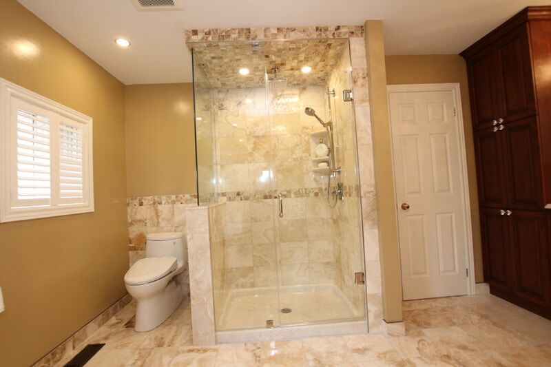 Modern bathroom design featuring a glass shower enclosure, marble tiles, beige walls, and a white toilet, showcasing Superior Bath's custom renovation work.