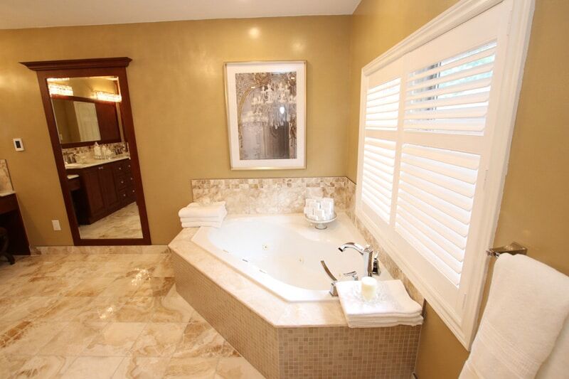 Luxurious bathroom featuring a modern corner jacuzzi tub, elegant beige walls, and a stylish mirror with a wooden frame, showcasing Superior Bath's custom renovation work.