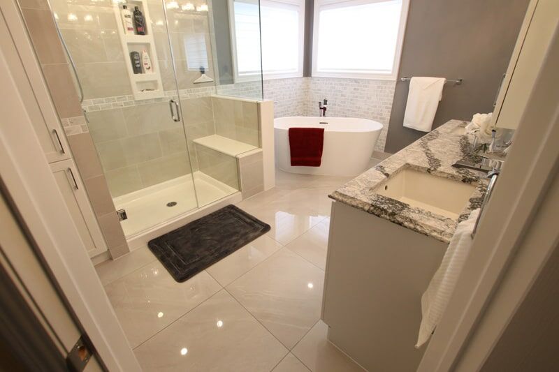 Modern bathroom featuring a glass shower, freestanding bathtub with red towel, and elegant granite countertop, showcasing Superior Bath's custom renovation work.