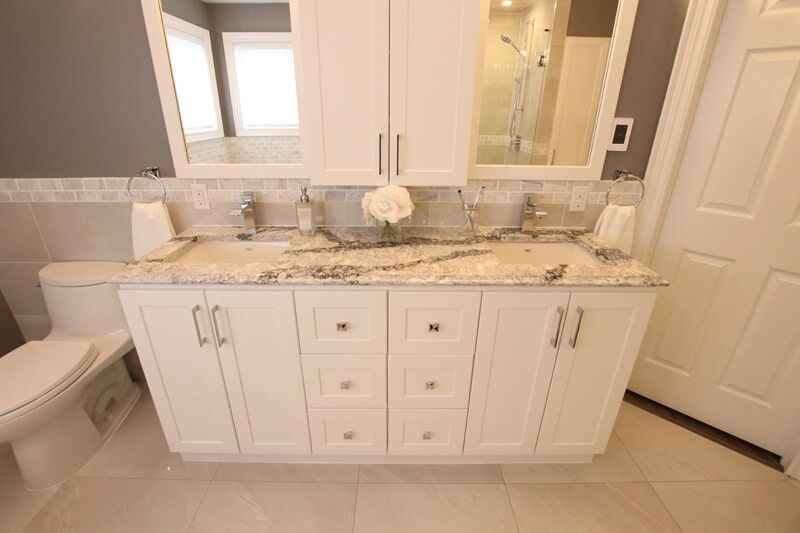 Modern bathroom vanity with white cabinetry, granite countertop, dual sinks, and decorative flower arrangement, showcasing Superior Bath's renovation craftsmanship.