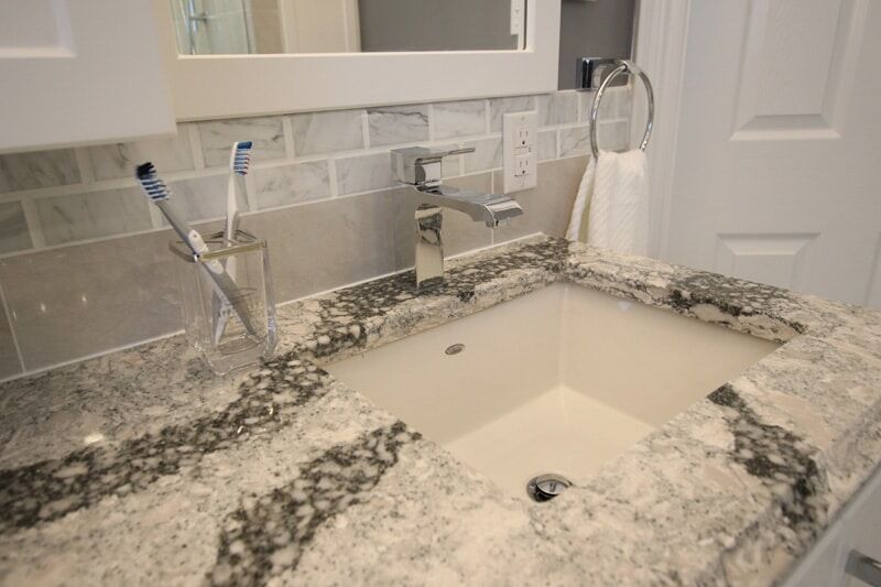 Modern bathroom sink with granite countertop, chrome faucet, toothbrush holder, and tiled backsplash, showcasing Superior Bath's custom renovation work.
