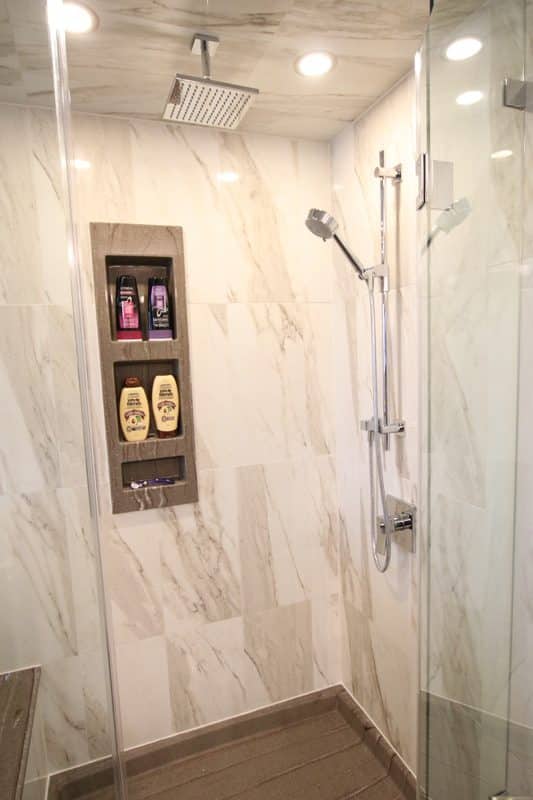 Modern shower with marble tiles, glass enclosure, overhead rain showerhead, and built-in storage for toiletries, showcasing Superior Bath's custom bathroom renovation design.
