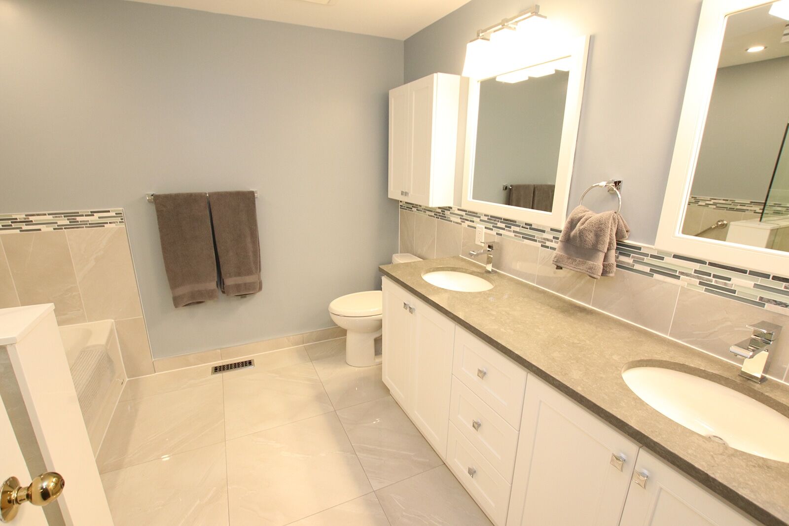 Modern bathroom renovation featuring dual sinks, gray stone countertop, white cabinetry, and stylish tile accents, showcasing Superior Bath's design capabilities.