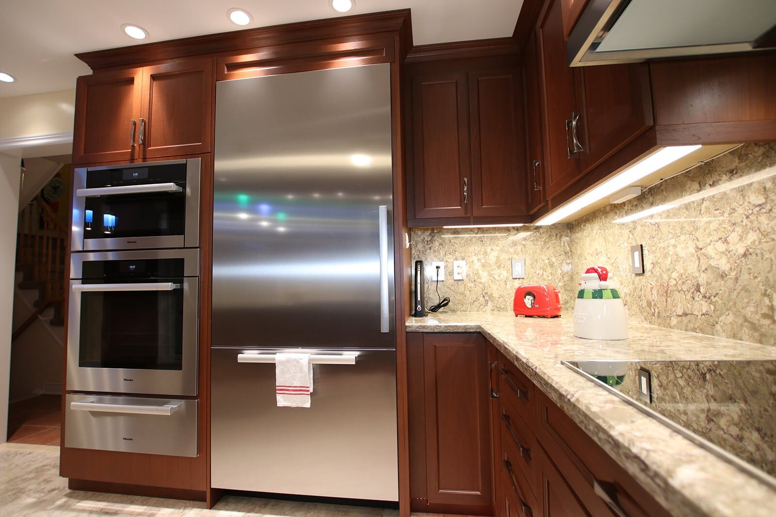 Modern kitchen featuring stainless steel refrigerator, built-in ovens, dark wood cabinetry, and granite countertop, showcasing Superior Bath's kitchen renovation expertise.