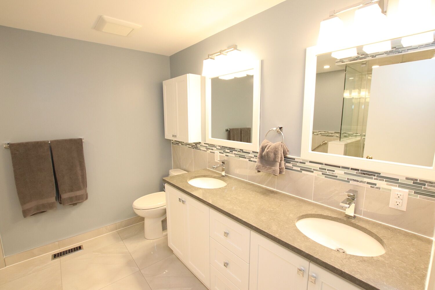Modern bathroom renovation featuring dual sinks, gray countertop, white cabinetry, and decorative tile backsplash, showcasing Superior Bath's craftsmanship.