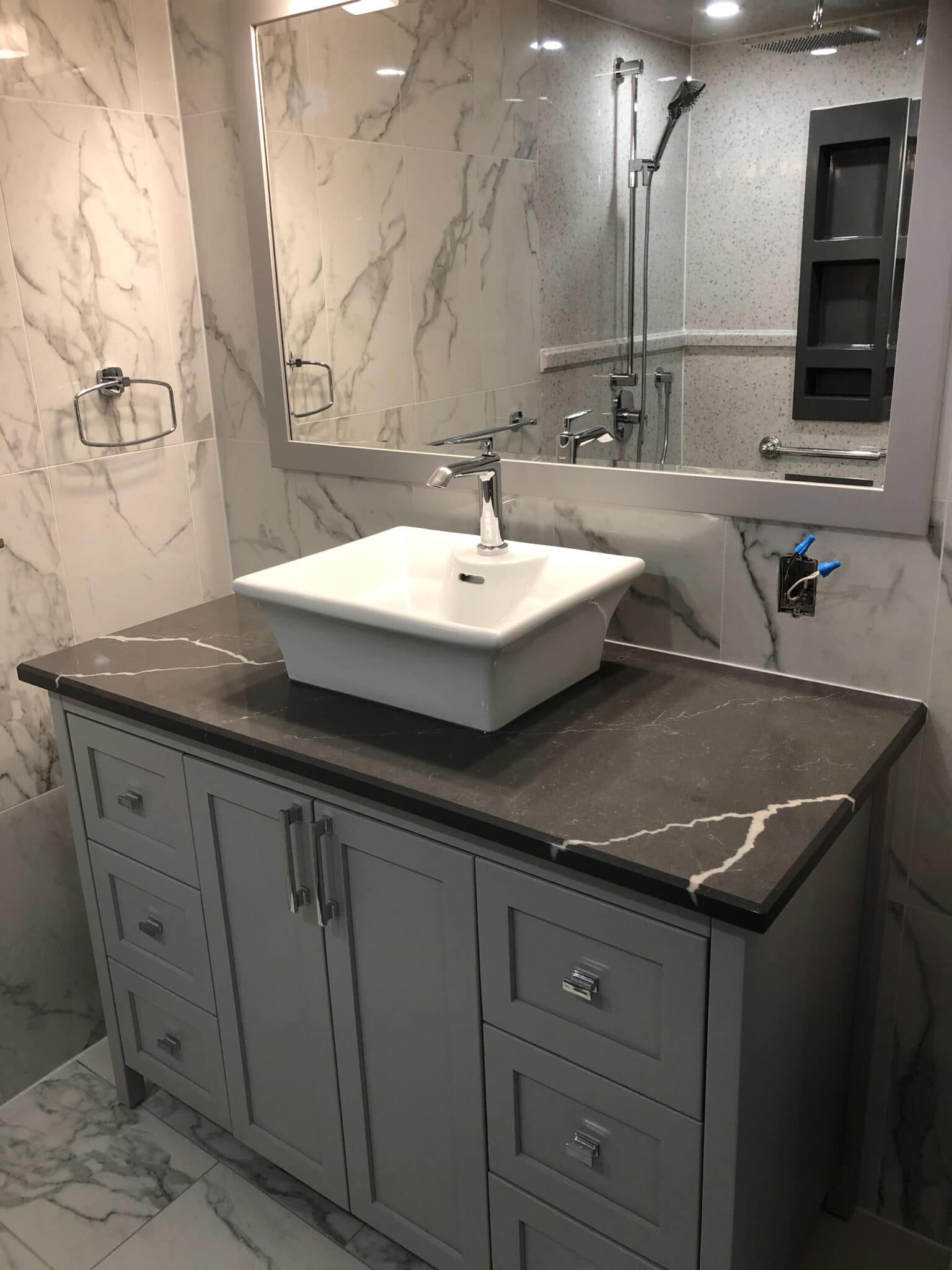 Modern bathroom design featuring a gray vanity with a black marble countertop, white vessel sink, large mirror, and marble wall tiles, showcasing Superior Bath's custom renovation craftsmanship.