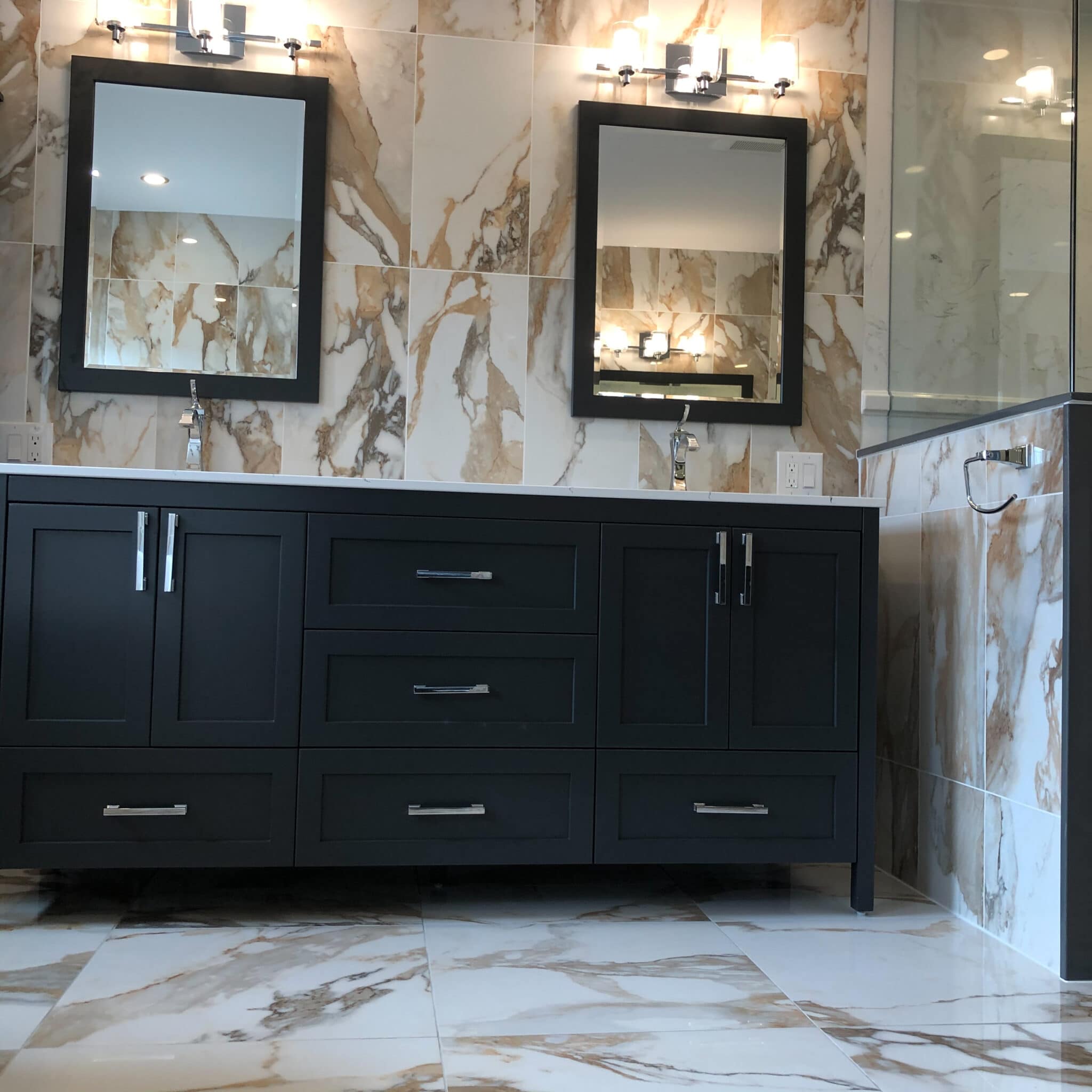 Custom bathroom renovation featuring a dark cabinetry vanity with dual mirrors, elegant marble wall tiles, and modern lighting fixtures, showcasing Superior Bath's craftsmanship.