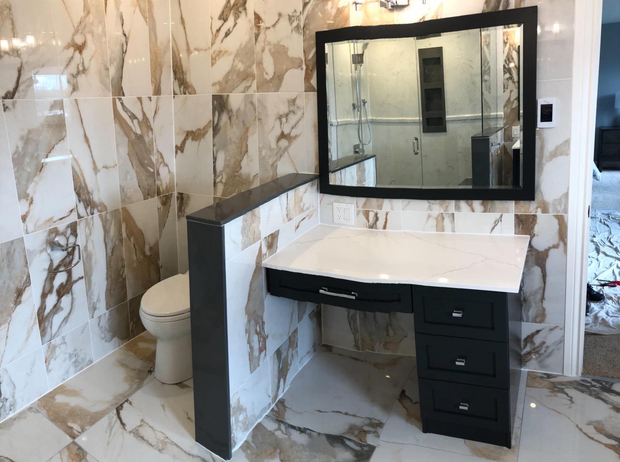 Modern bathroom renovation featuring elegant marble tile walls, a sleek black vanity with a white countertop, and a large mirror, showcasing Superior Bath's custom design capabilities.