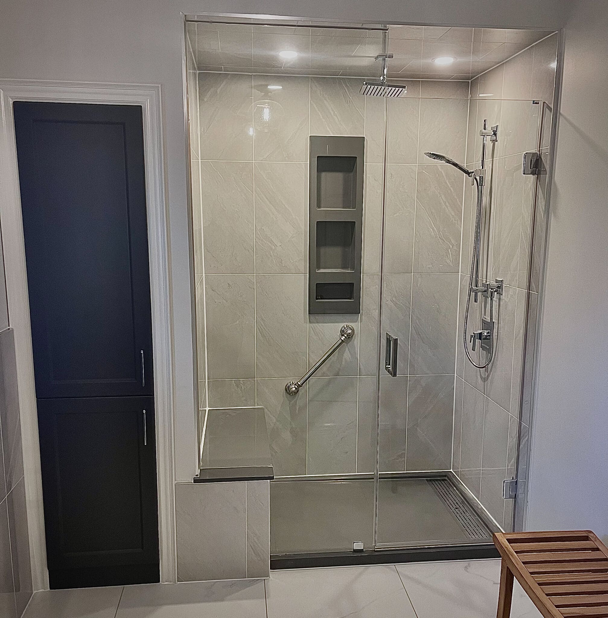 Modern shower with frameless glass doors, rainfall showerhead, built-in storage niche, and grab bar, showcasing a sleek design for tub-to-shower conversions.