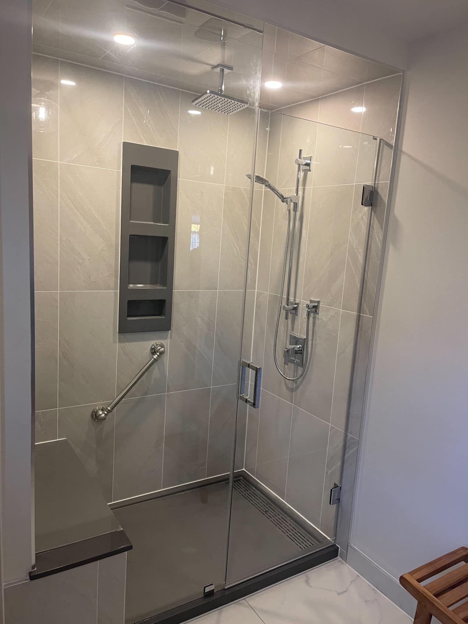 Modern glass shower enclosure featuring sleek gray tiles, built-in shelving, and contemporary fixtures, showcasing Superior Bath's custom bathroom renovation expertise.