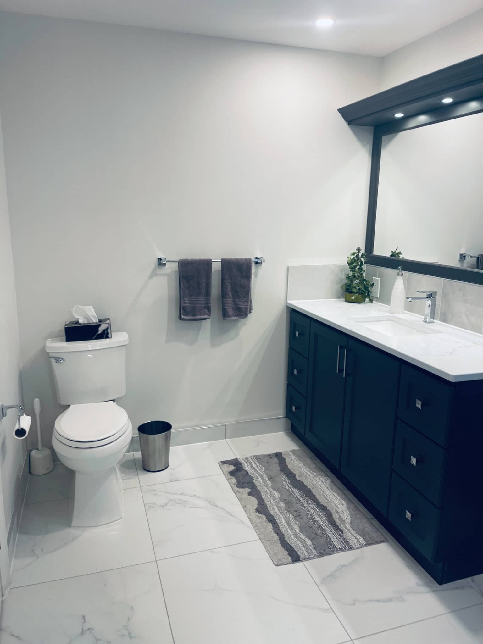 Modern bathroom renovation featuring a dark cabinetry, white marble countertop, gray towels, and decorative plant, showcasing Superior Bath's craftsmanship.