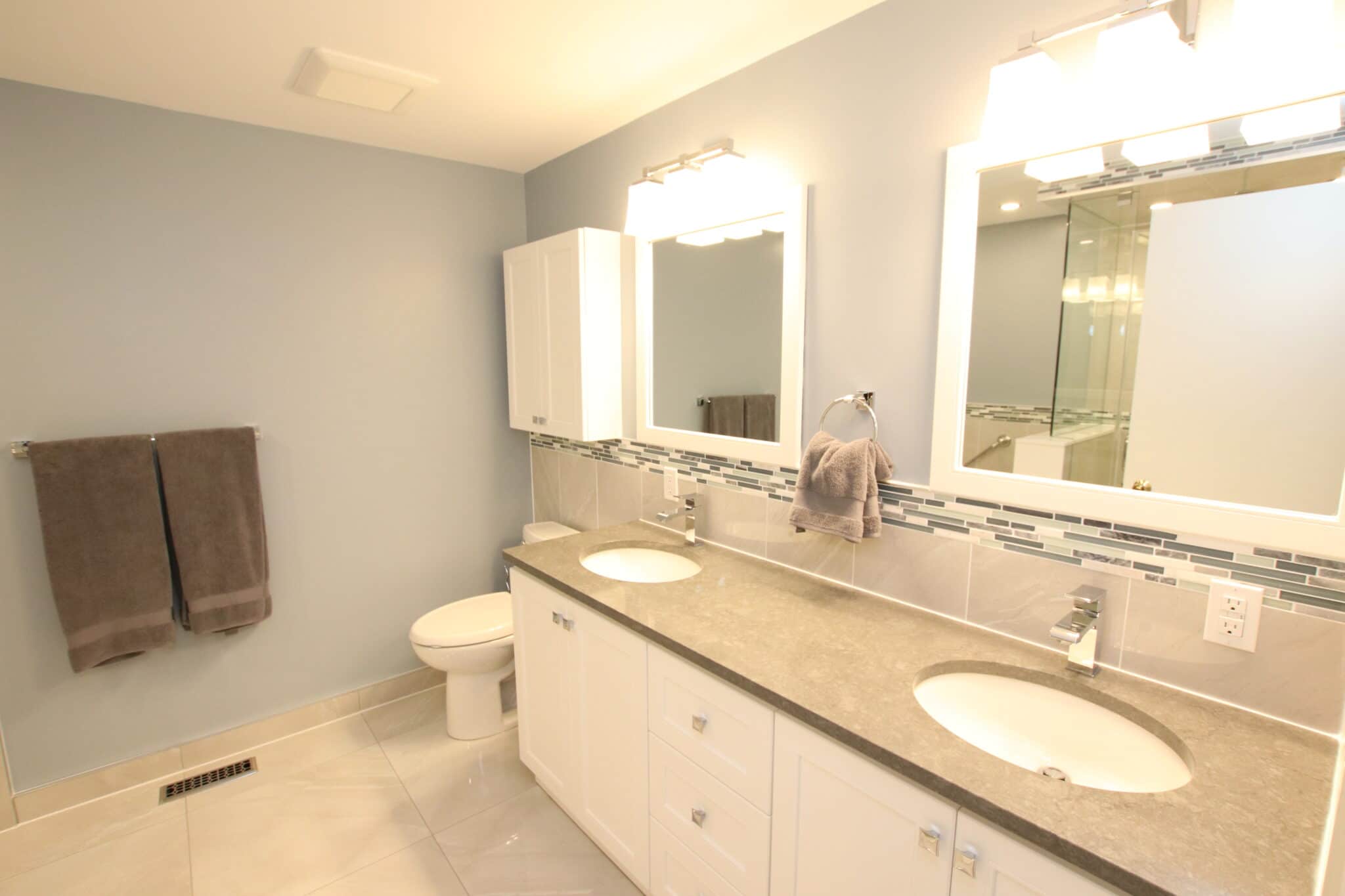 Modern bathroom renovation featuring dual sinks, gray countertop, white cabinetry, and stylish mirrors, showcasing Superior Bath's craftsmanship.