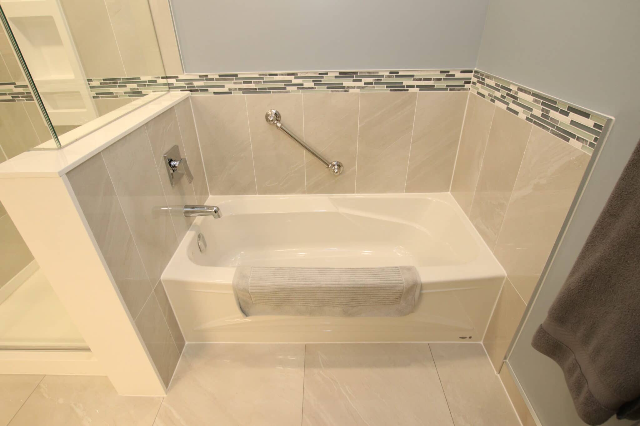 Custom bathroom renovation featuring a modern bathtub with a decorative tile backsplash, chrome fixtures, and a soft towel, showcasing Superior Bath's craftsmanship.