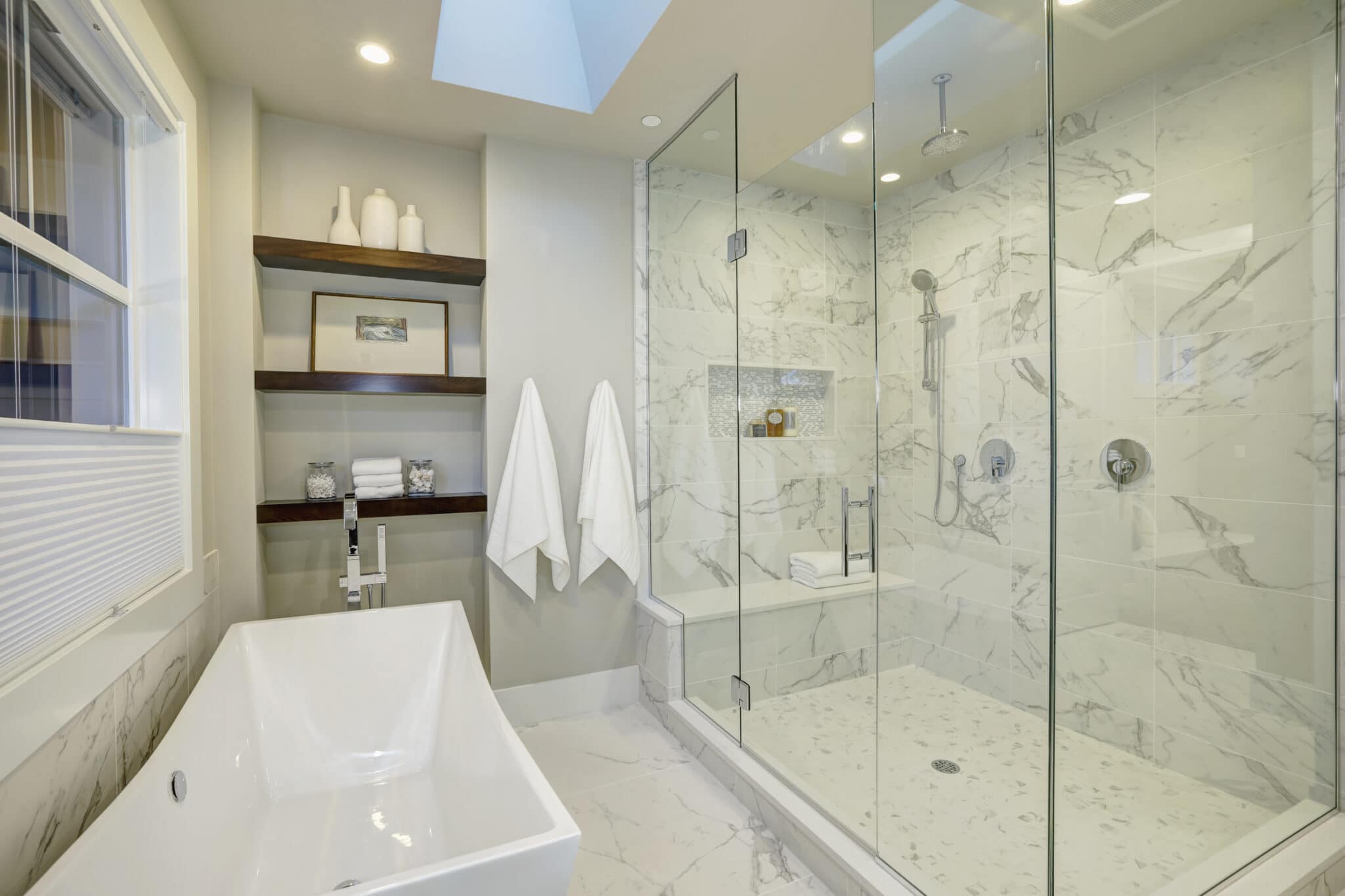 Modern bathroom design featuring a freestanding tub, glass shower enclosure, marble walls, and wooden shelving with decorative items, showcasing Superior Bath's custom renovation capabilities.