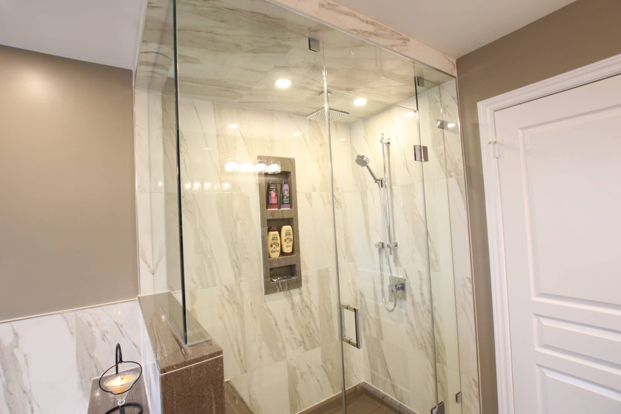 Modern glass shower enclosure featuring marble walls, built-in shelf with shampoo and body wash, and contemporary fixtures, showcasing Superior Bath's custom bathroom renovation design.