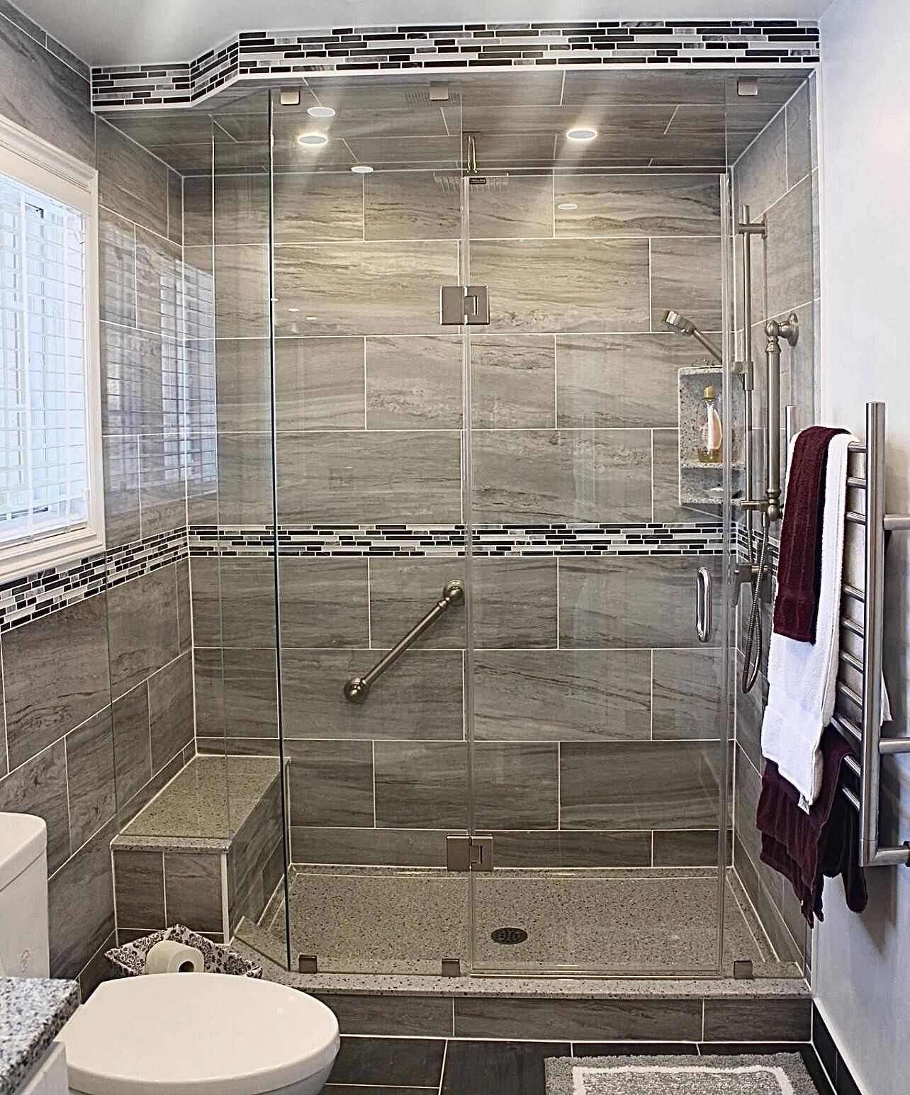 Modern bathroom renovation featuring a glass shower enclosure, gray tile walls, a built-in bench, and stylish accents, showcasing Superior Bath's craftsmanship.