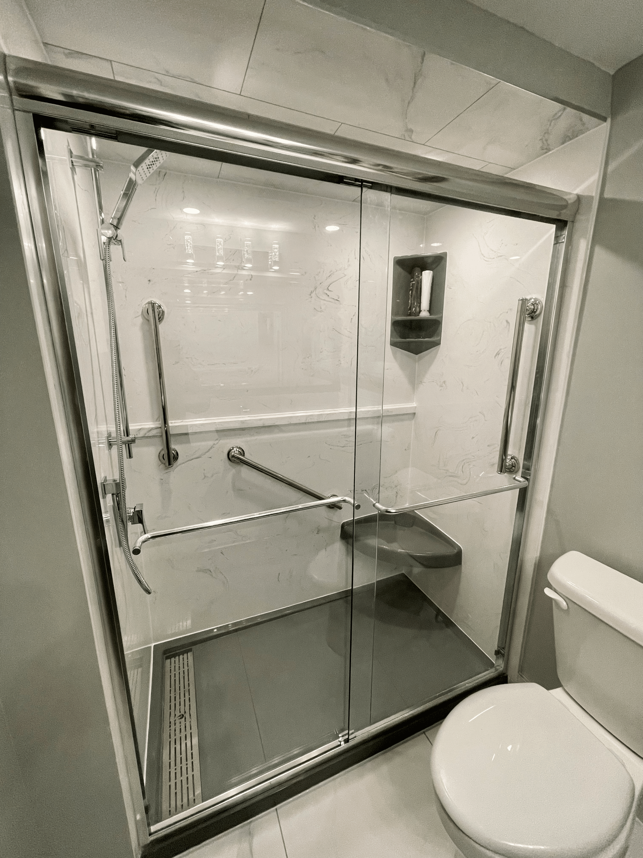 Modern glass shower enclosure with grab bars, marble walls, and sleek fixtures in a renovated bathroom, showcasing Superior Bath's custom design expertise.