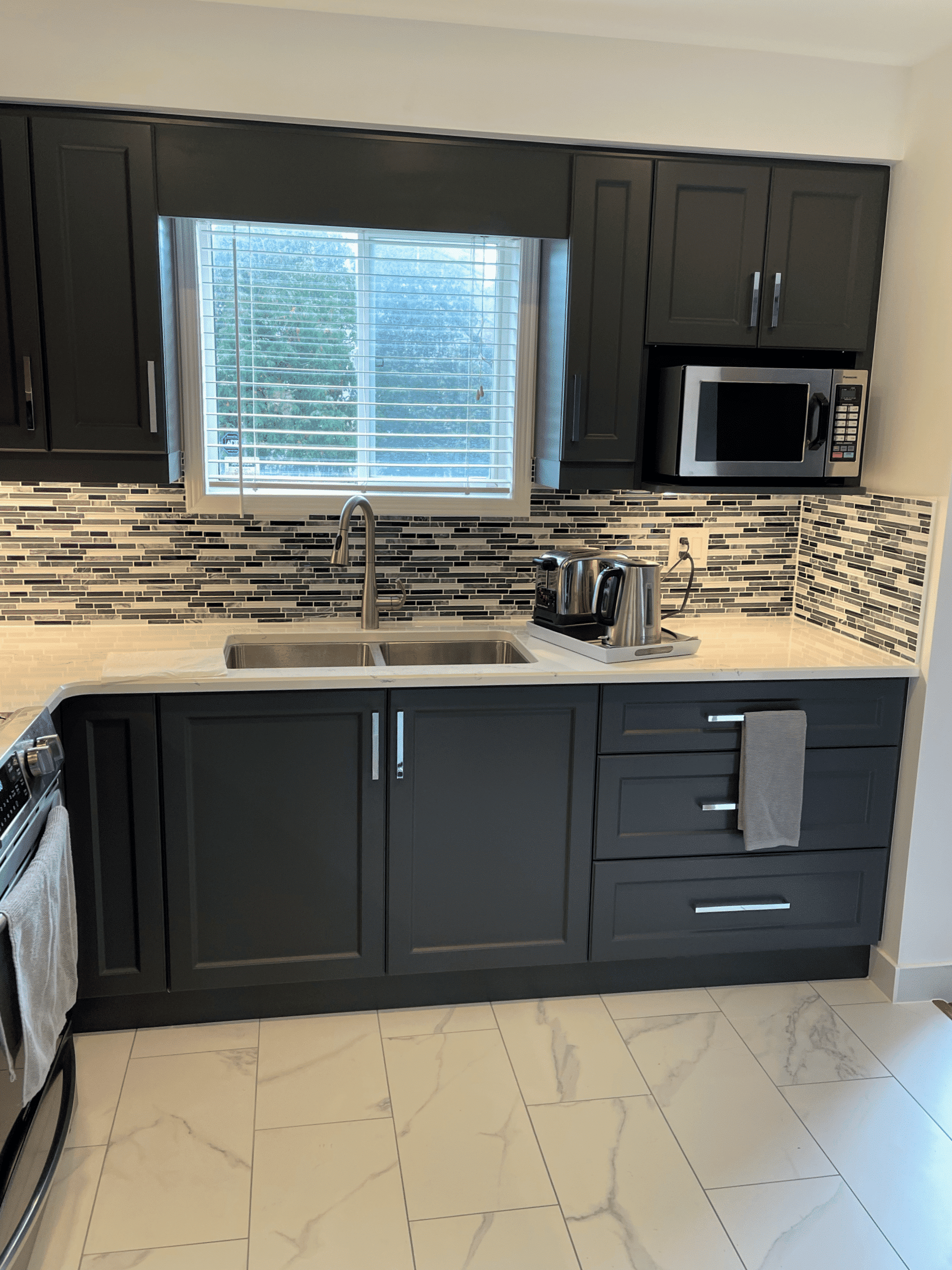 Modern kitchen featuring dark cabinetry, stainless steel appliances, dual sink, and mosaic tile backsplash, ideal for renovation inspiration by Superior Bath.