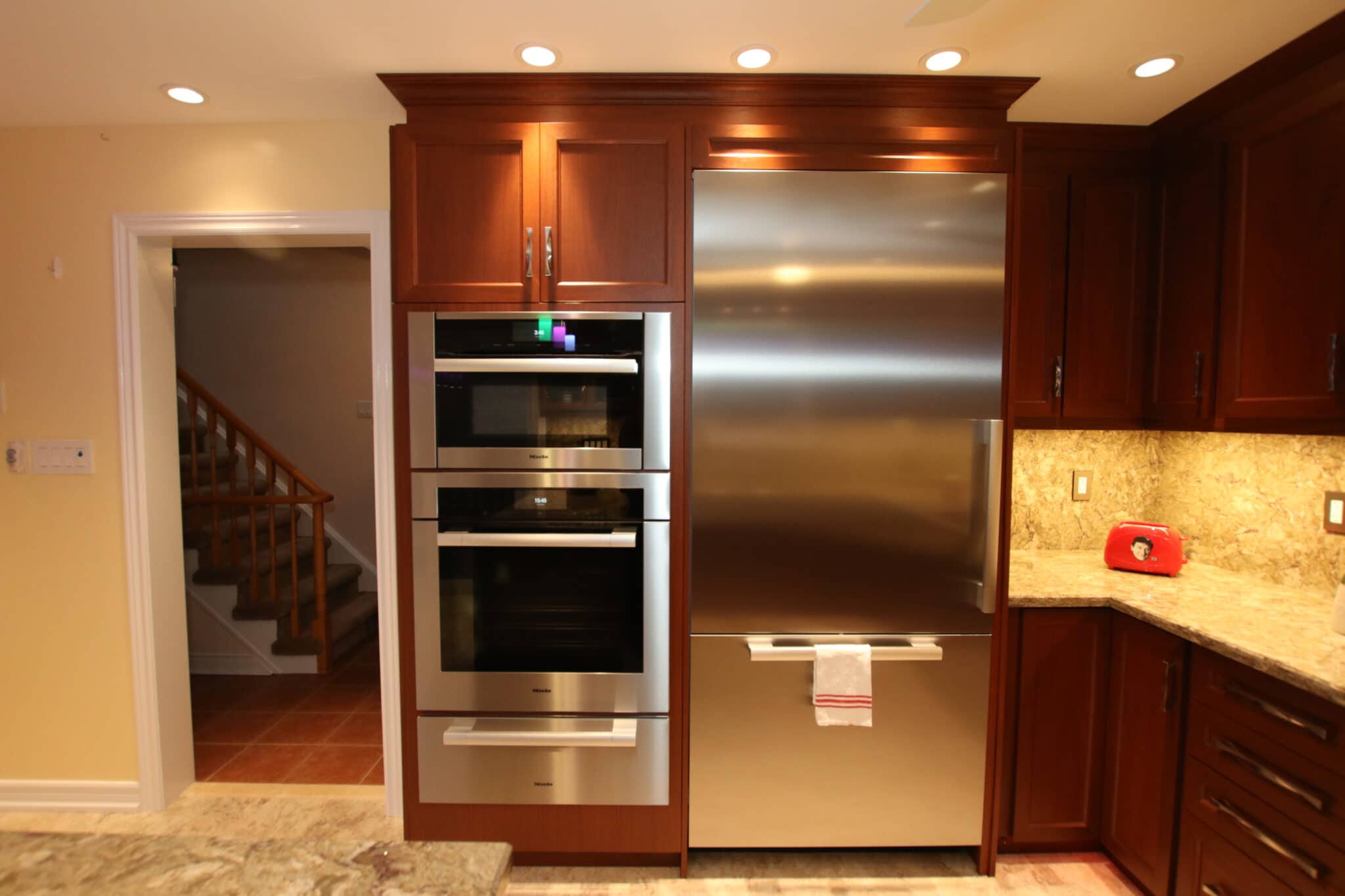 Modern kitchen featuring stainless steel refrigerator, built-in ovens, wooden cabinetry, and granite countertops, showcasing Superior Bath's renovation expertise.