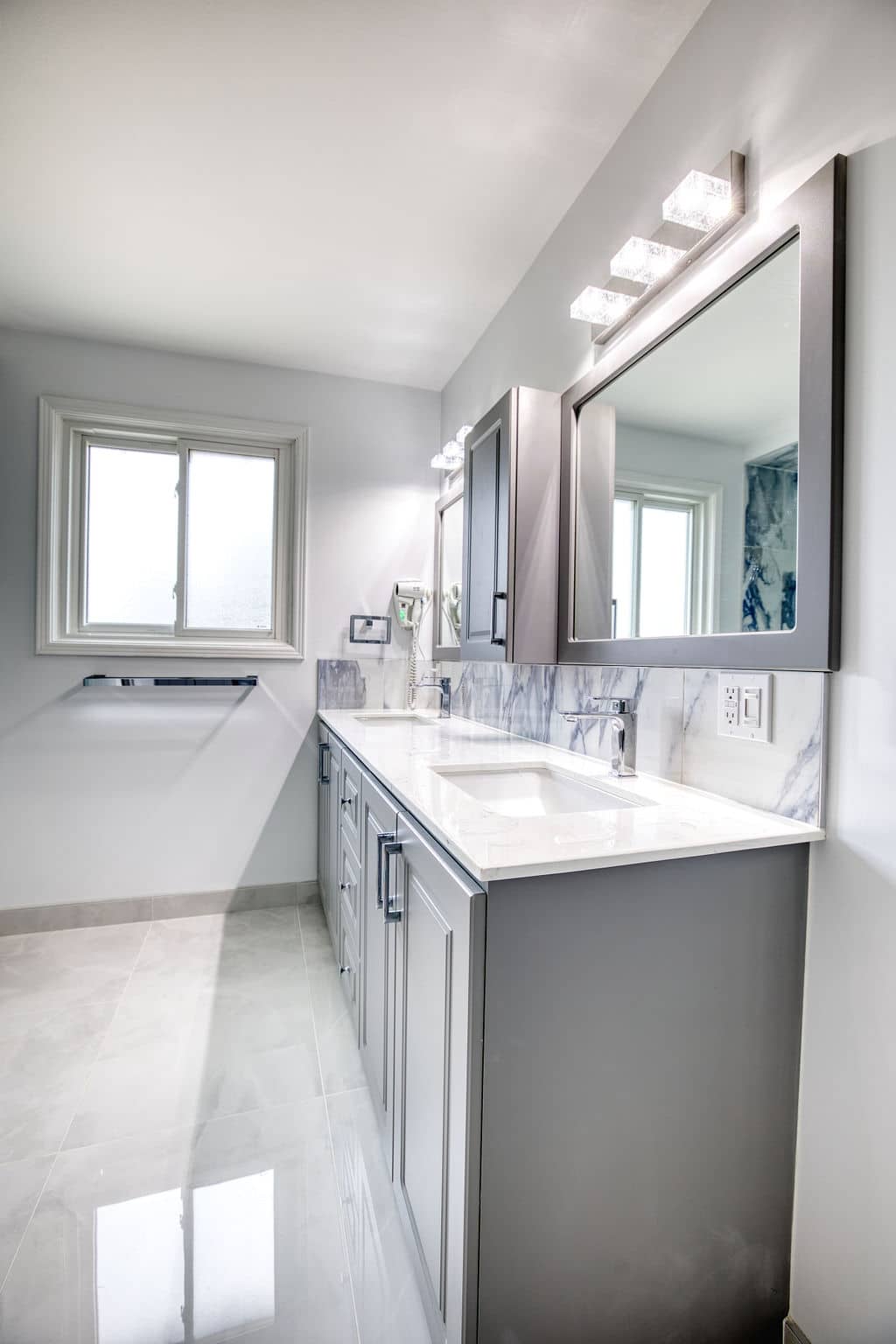 Modern bathroom design featuring a sleek gray vanity with dual sinks, marble countertop, contemporary mirrors, and natural light from a window, showcasing Superior Bath's custom renovation craftsmanship.