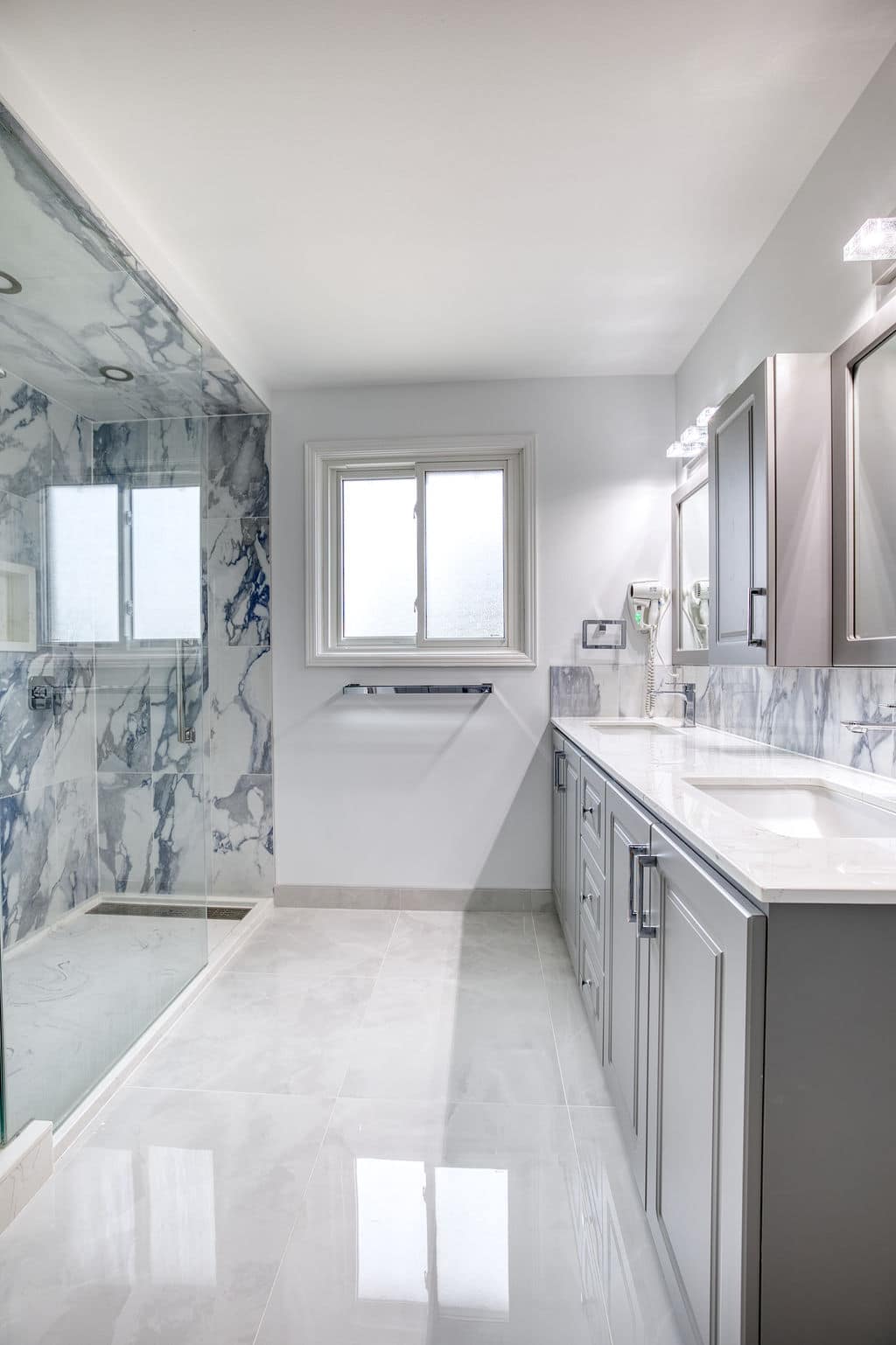 Modern bathroom renovation featuring marble walls, glass shower enclosure, sleek cabinetry, and dual sinks by Superior Bath.