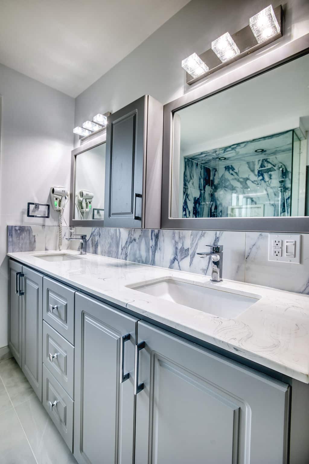 Custom bathroom with gray cabinetry, marble countertop, dual sinks, modern lighting, and elegant mirrors, showcasing a luxurious and functional design by Superior Bath Reno.