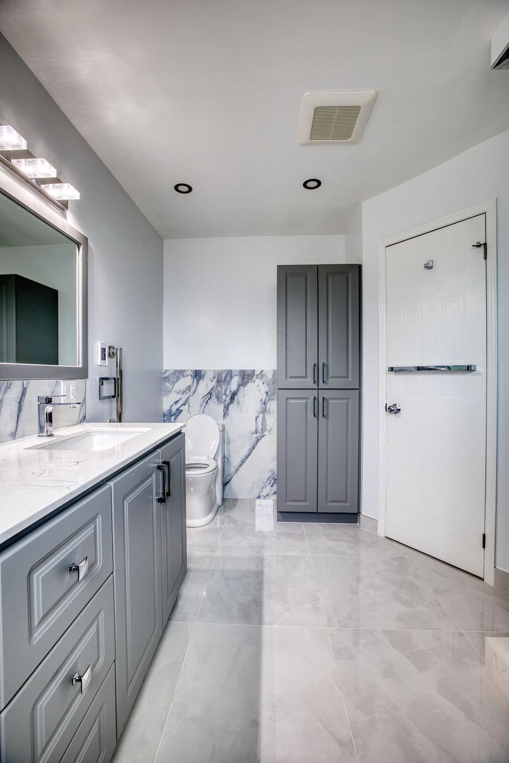Modern bathroom interior featuring gray cabinetry, marble backsplash, white porcelain toilet, and sleek lighting, showcasing Superior Bath's custom renovation design.