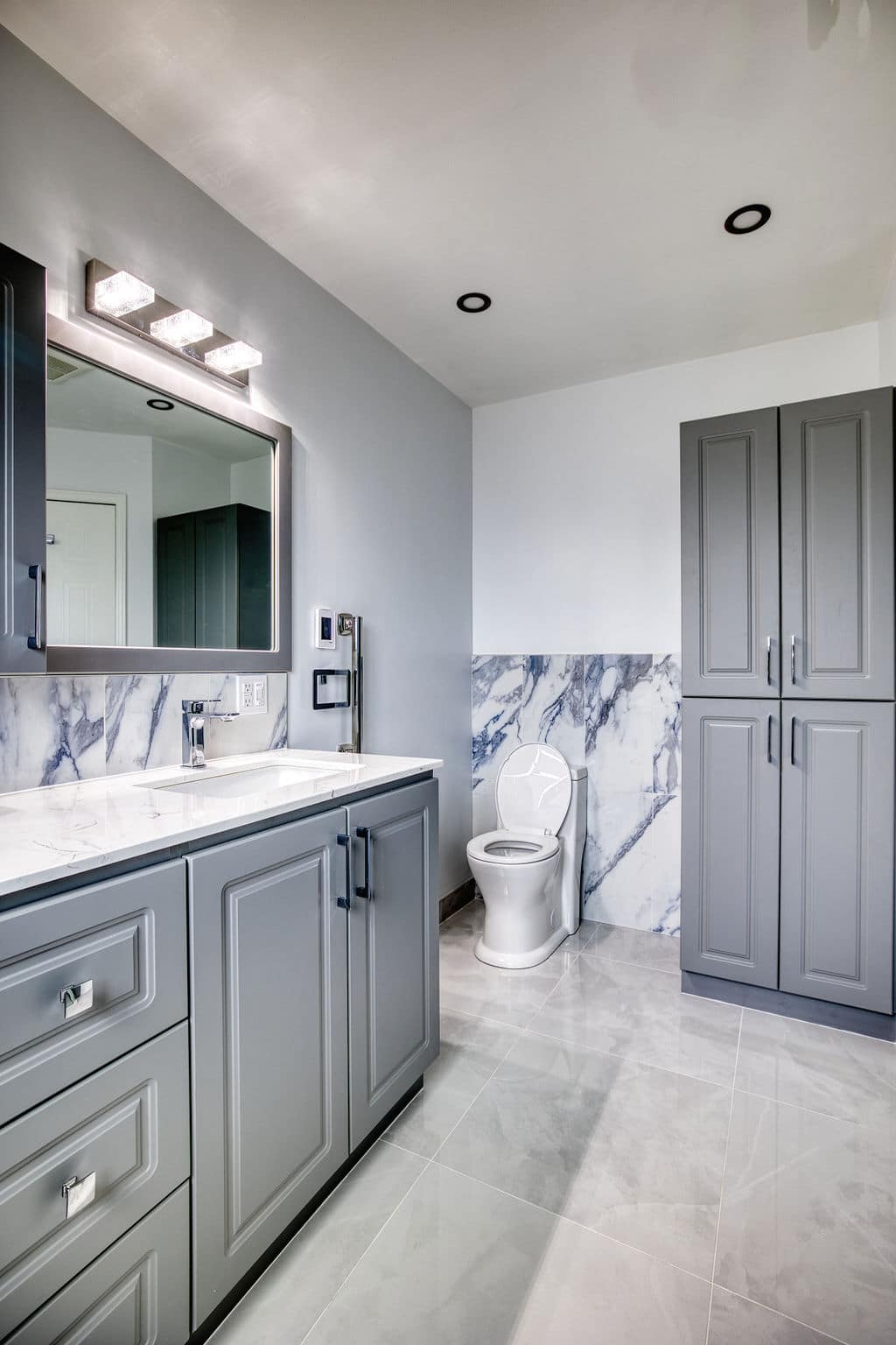 Modern bathroom design featuring gray cabinetry, marble accents, sleek mirror with lighting, and a white toilet, showcasing Superior Bath Reno's custom renovation expertise.