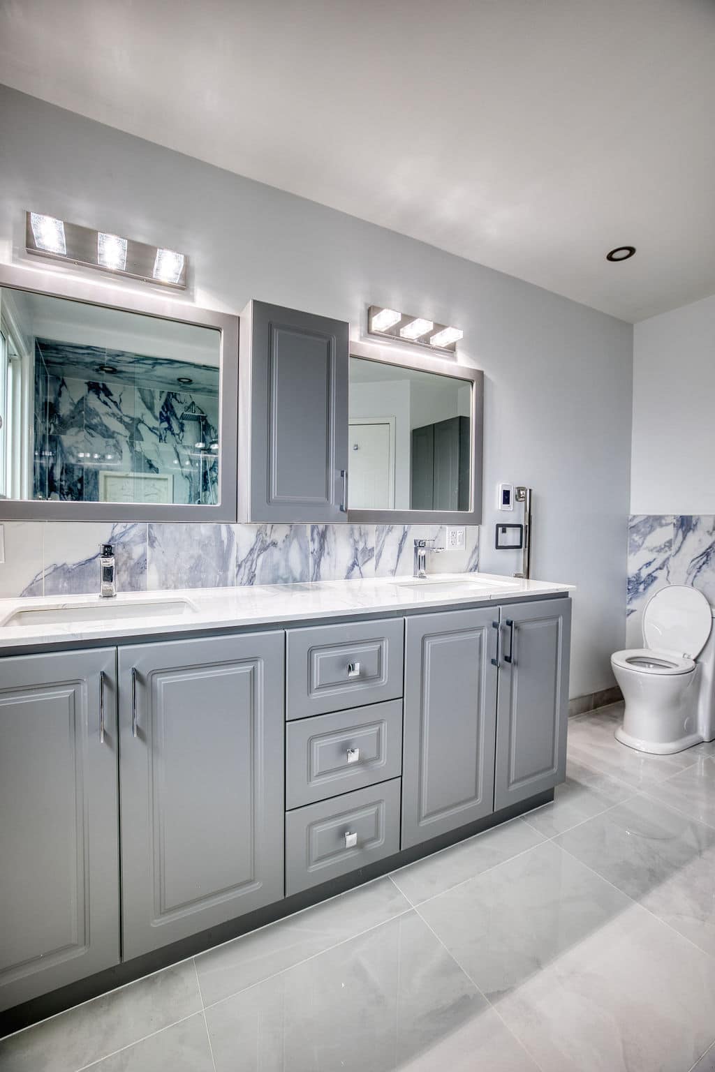 Modern bathroom renovation featuring a grey vanity with double sinks, marble backsplash, and contemporary lighting, showcasing Superior Bath's design expertise.