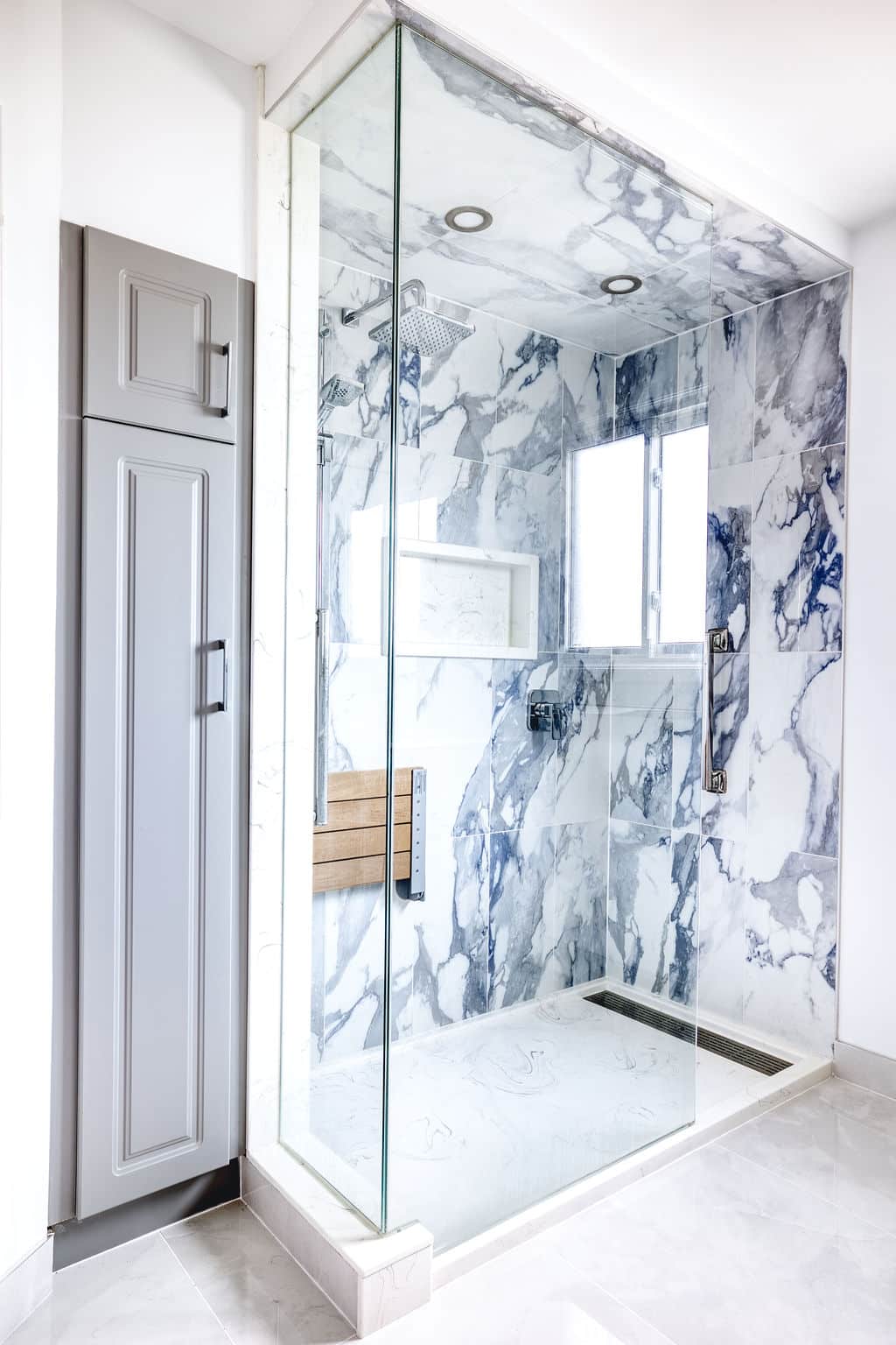 Custom bathroom renovation featuring a modern glass shower with marble-patterned tiles, wooden bench, and elegant fixtures, showcasing Superior Bath's craftsmanship.