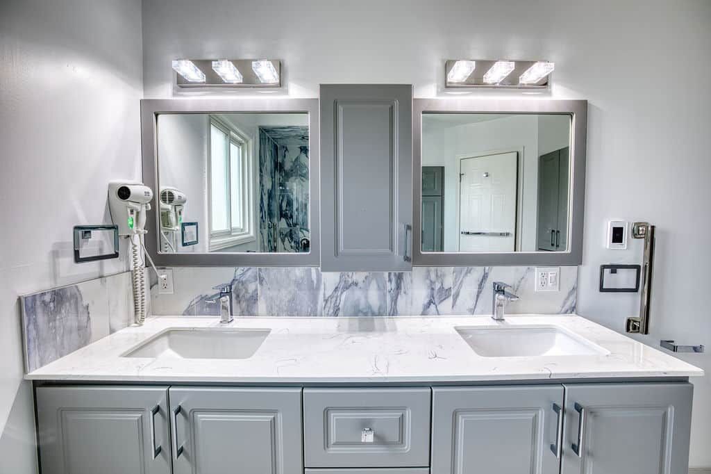 Modern bathroom vanity with dual sinks, gray cabinetry, marble backsplash, and illuminated mirrors, showcasing Superior Bath's custom renovation design.