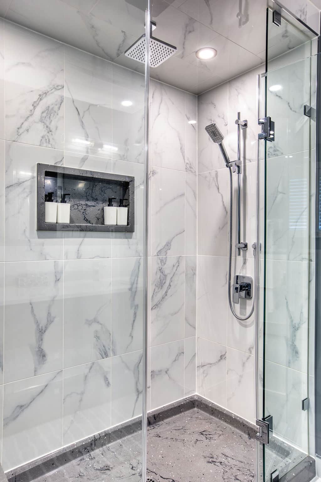 Modern bathroom shower featuring elegant marble tiles, glass enclosure, and built-in shelf with toiletries, showcasing Superior Bath's custom renovation craftsmanship.
