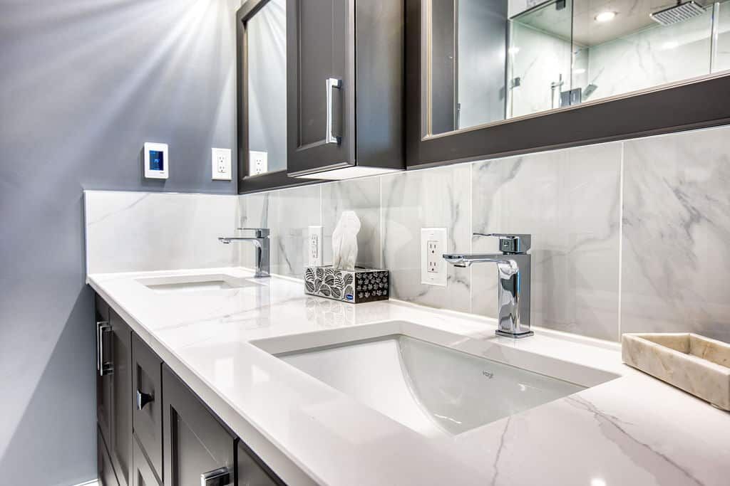 Custom bathroom vanity with dual sinks, modern fixtures, marble countertop, and stylish cabinetry in a renovated space.