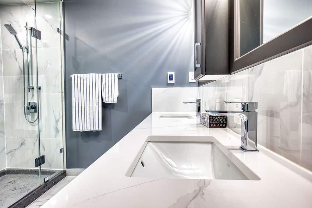 Modern bathroom design featuring sleek marble countertop, dual chrome faucets, glass shower enclosure, and striped towels, showcasing Superior Bath's custom renovation craftsmanship.