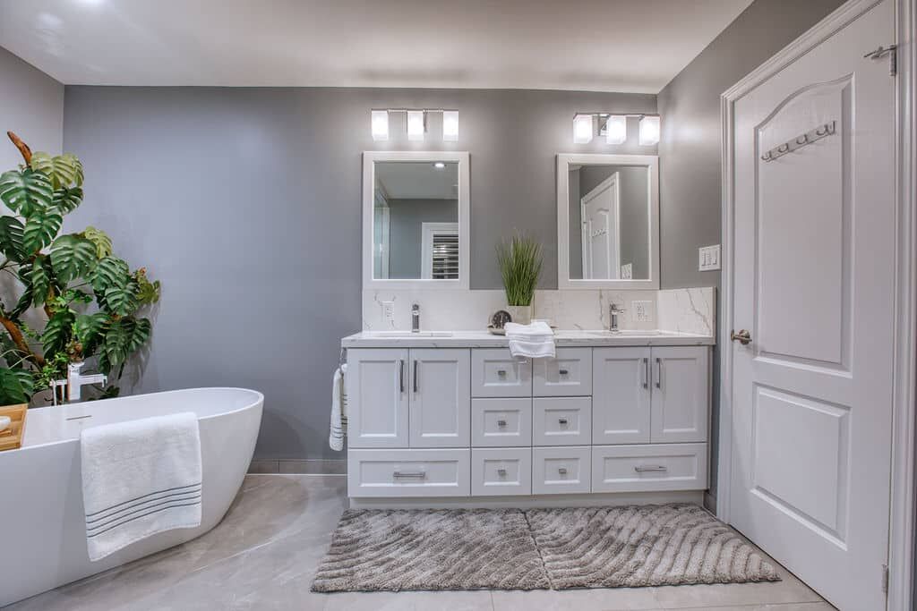 Modern custom bathroom featuring a sleek white freestanding bathtub, dual mirrors above a stylish vanity with storage, and a potted plant, showcasing Superior Bath's renovation expertise.