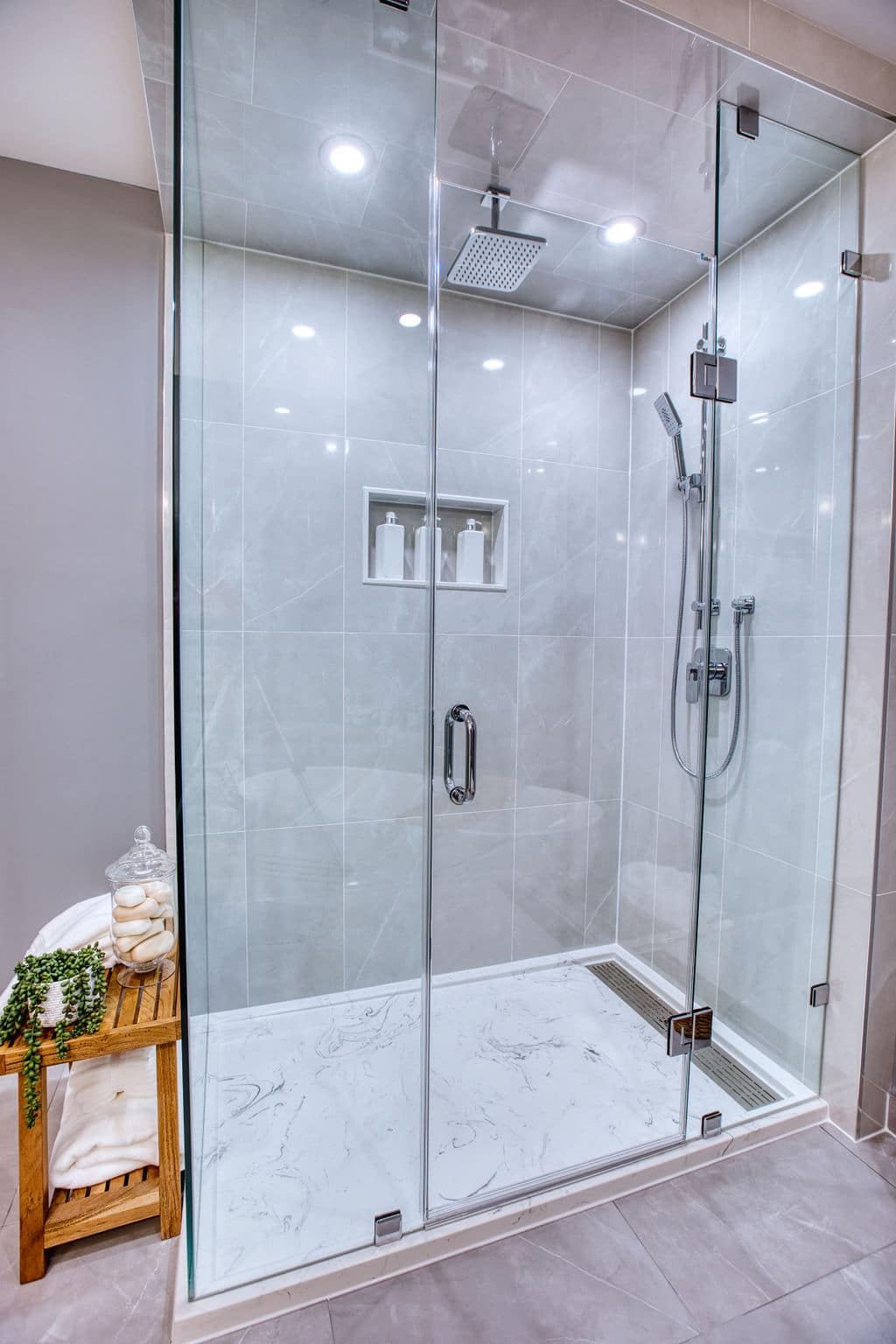 Modern glass shower enclosure featuring a rainfall showerhead, sleek tile design, and built-in shelving with toiletries, showcasing Superior Bath's custom bathroom renovation expertise.