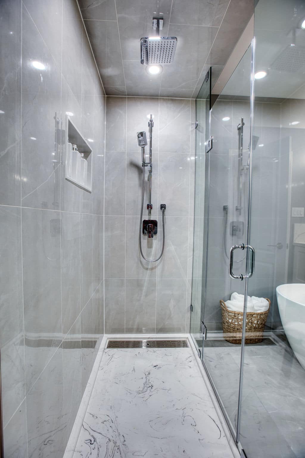 Modern glass shower enclosure with rainfall showerhead, sleek marble flooring, and built-in shelf for toiletries, showcasing Superior Bath's custom bathroom renovation design.