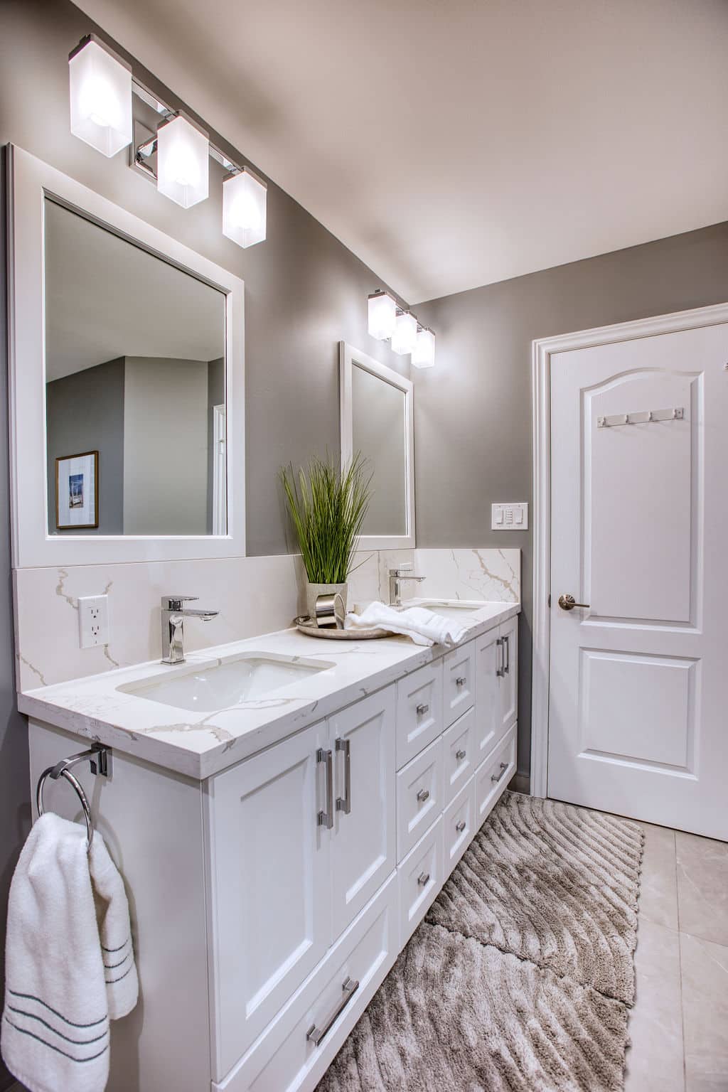 Modern bathroom design featuring a double vanity with white cabinetry, marble countertop, stylish lighting fixtures, and decorative plant, showcasing Superior Bath's custom renovation work.