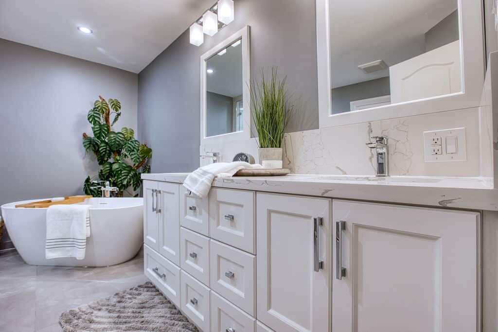 Modern bathroom with white cabinetry, marble countertop, and stylish fixtures, featuring a freestanding tub, decorative plant, and elegant lighting, showcasing Superior Bath's custom renovation work.
