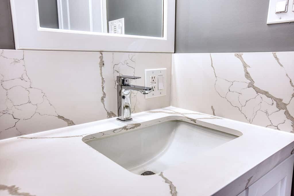 Modern bathroom vanity with sleek faucet, white countertop featuring elegant marble pattern, and mirror above, showcasing Superior Bath's custom renovation style.