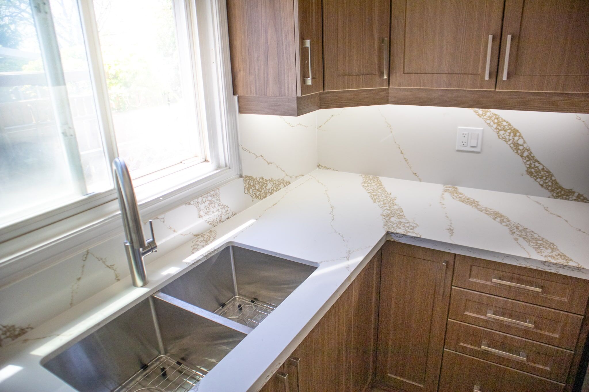 Modern kitchen renovation featuring a sleek stainless steel sink, elegant white countertop with gold veining, and warm wood cabinetry, showcasing Superior Bath's design expertise.