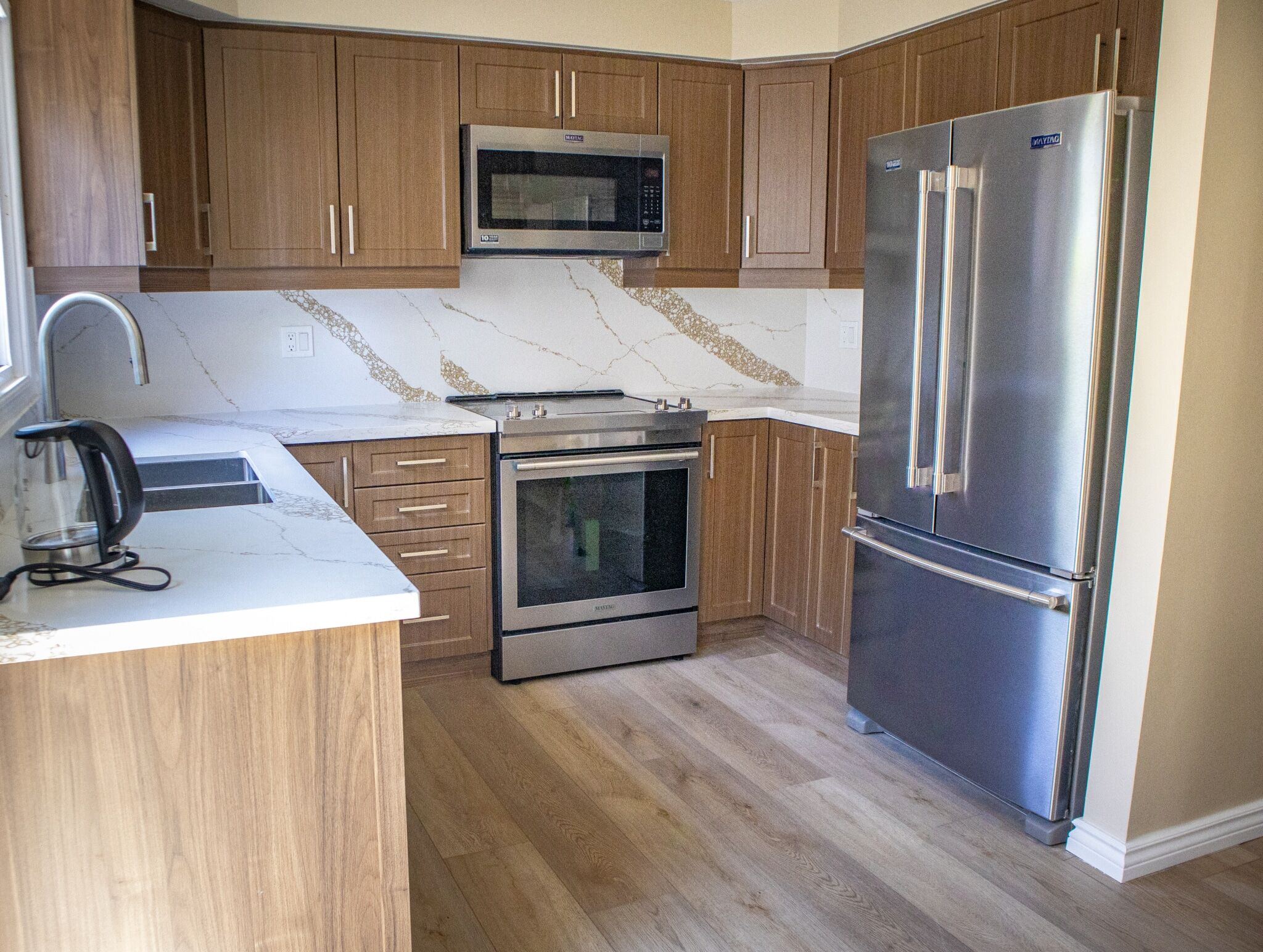 Modern kitchen renovation featuring wood cabinetry, stainless steel appliances, quartz countertop with veining, and a sleek design by Superior Bath.