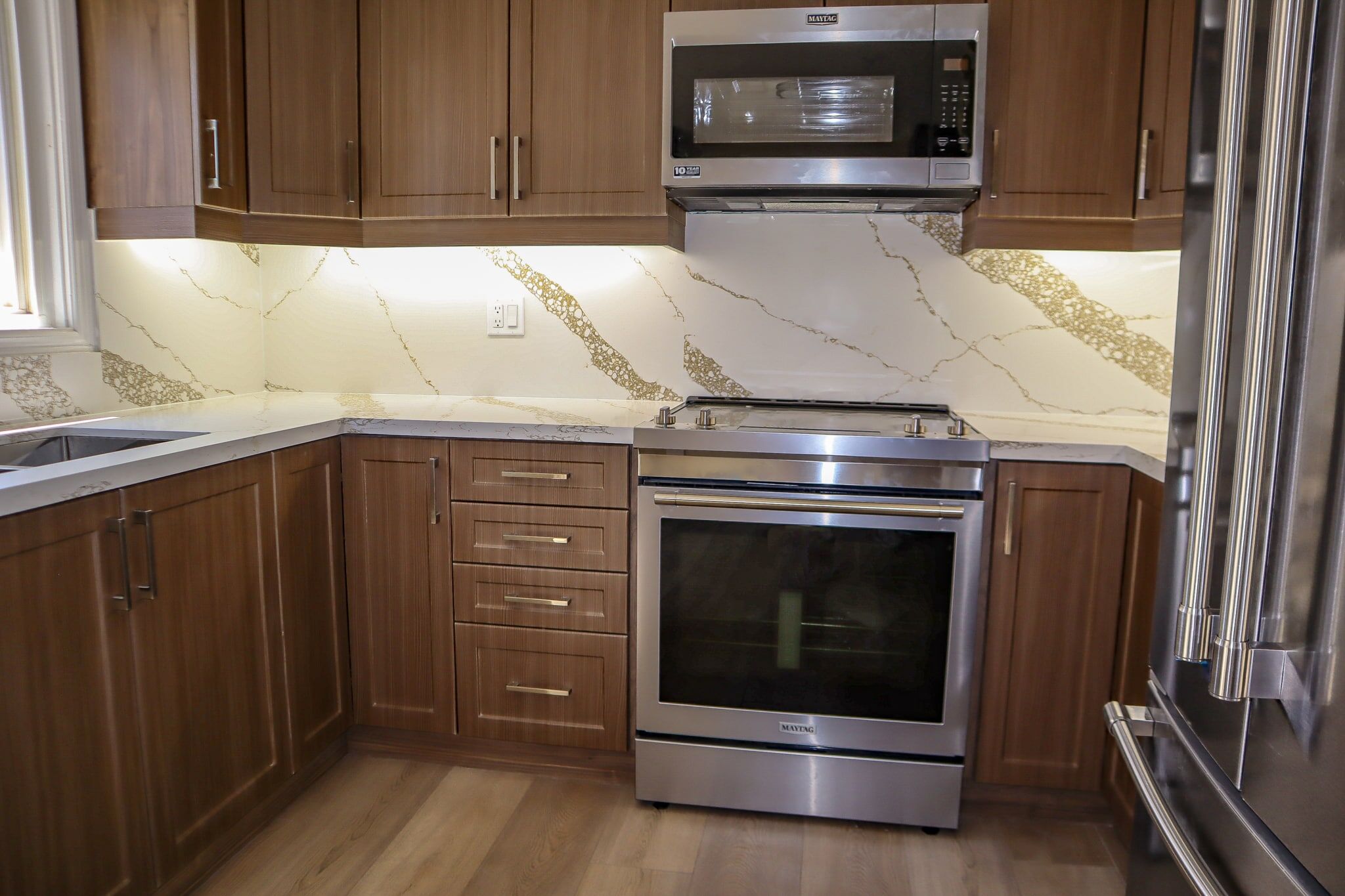 Modern kitchen featuring wooden cabinets, stainless steel oven and microwave, and elegant marble backsplash with gold veining.