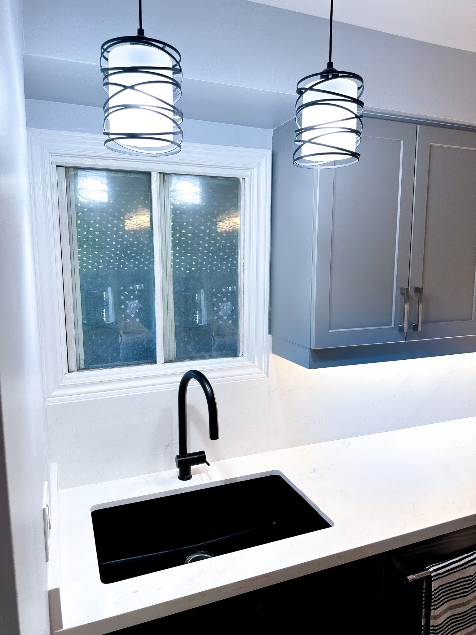Modern kitchen sink with black faucet, white countertop, and stylish pendant lighting, showcasing Superior Bath's kitchen renovation design.