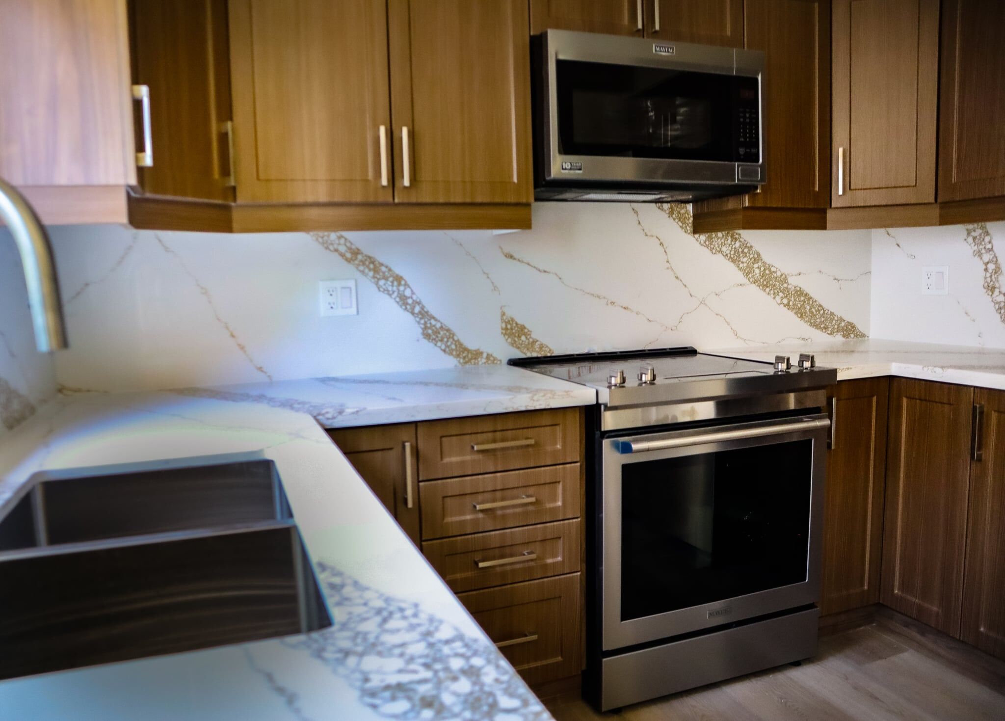 Modern kitchen with wooden cabinets, marble countertops, stainless steel oven and microwave, showcasing a stylish renovation by Superior Bath.
