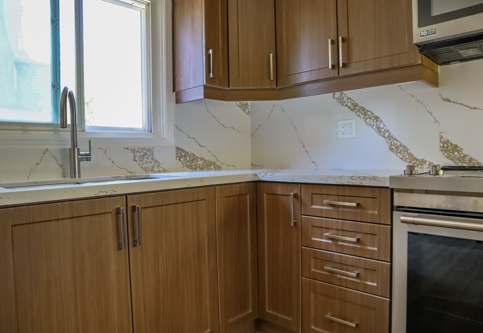Modern kitchen with wooden cabinetry, marble countertop featuring gold veining, stainless steel sink, and window providing natural light, showcasing Superior Bath's renovation expertise.