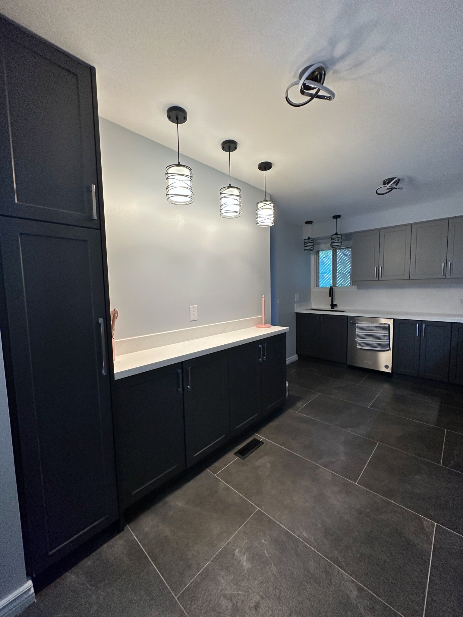 Modern kitchen renovation featuring sleek black cabinetry, stylish pendant lighting, and a spacious layout with gray tile flooring, showcasing Superior Bath's design expertise.