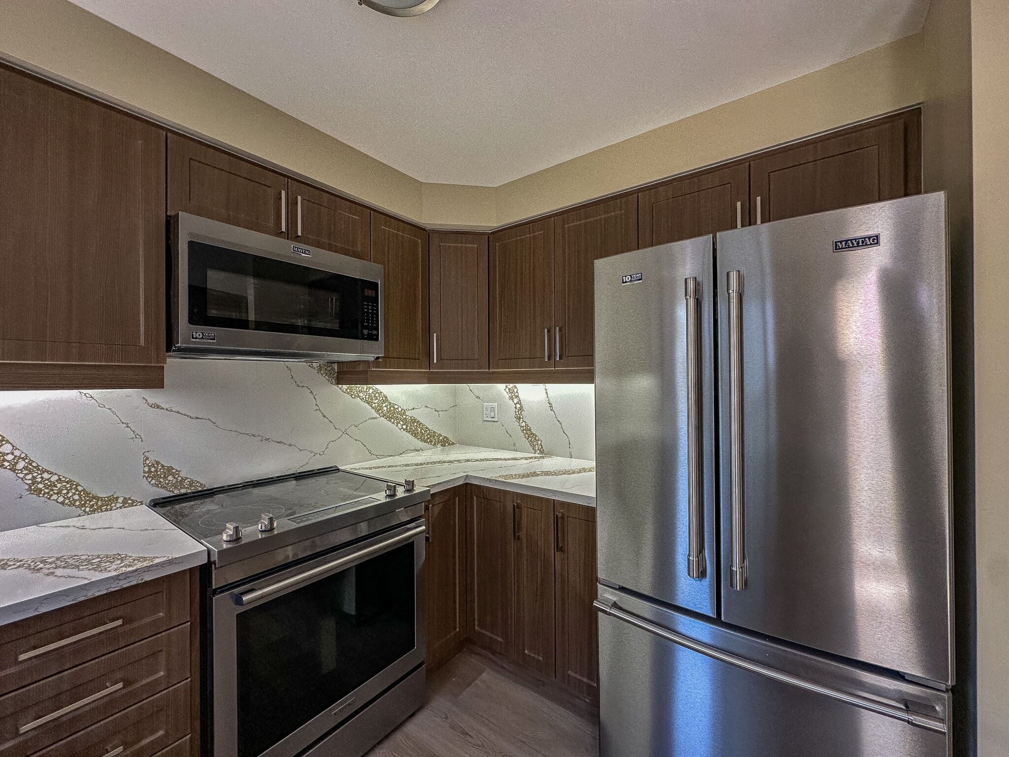 Modern kitchen renovation featuring dark wood cabinetry, stainless steel appliances, and a marble backsplash with gold accents, showcasing Superior Bath's design expertise.