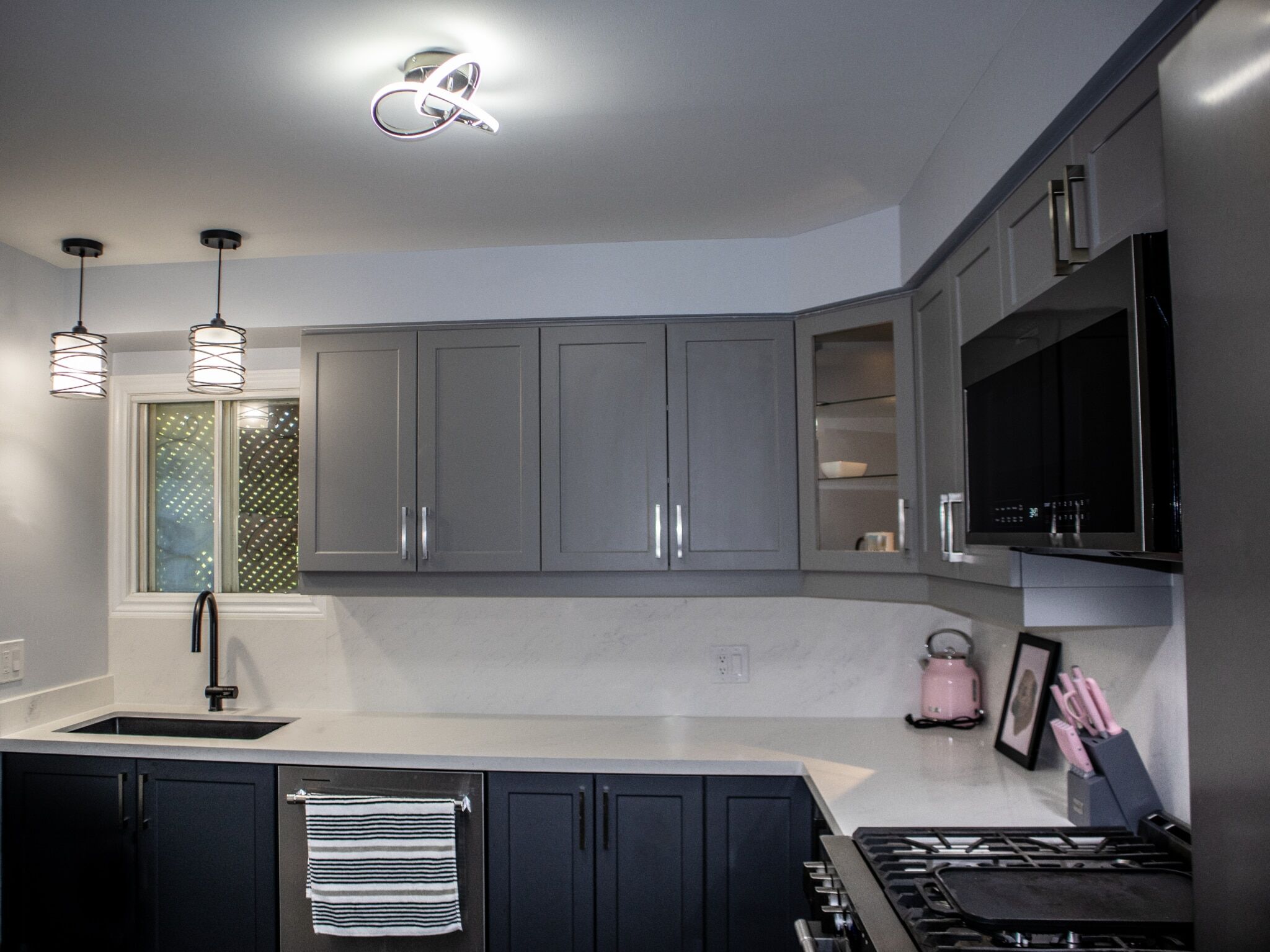 Modern kitchen with gray cabinetry, sleek countertops, pendant lighting, and stainless steel appliances, showcasing Superior Bath's renovation style.