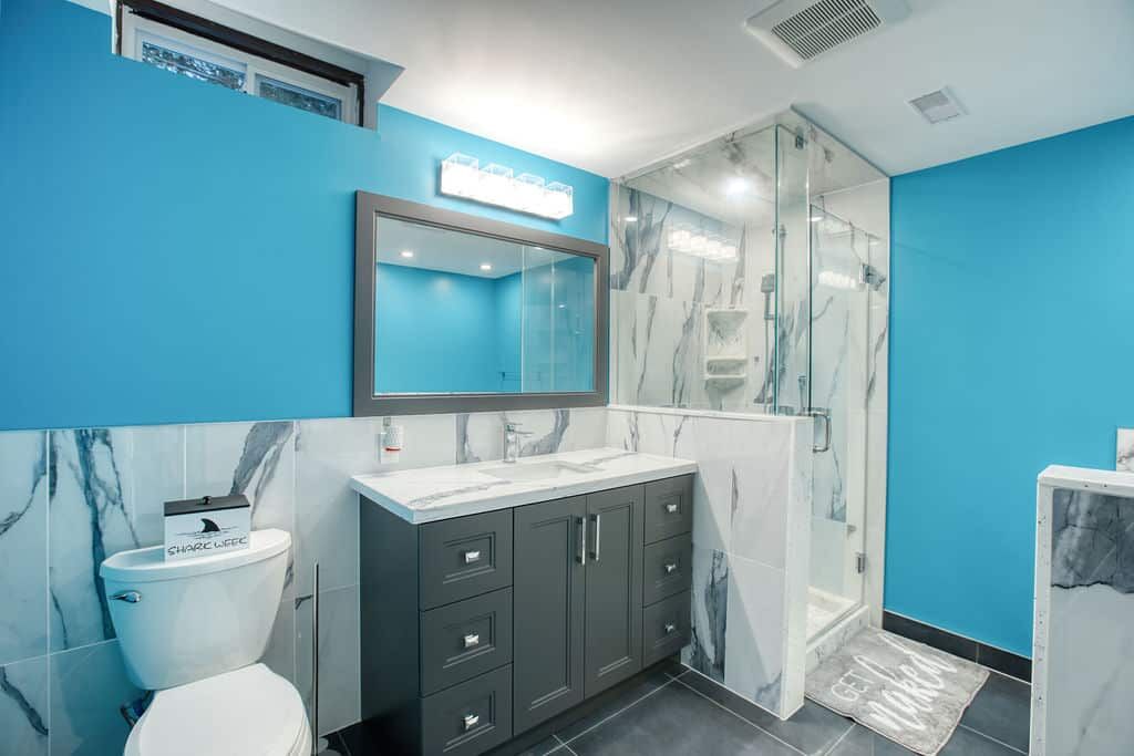 Custom bathroom renovation featuring a modern design with blue walls, marble accents, a sleek vanity with storage, and a glass shower enclosure.